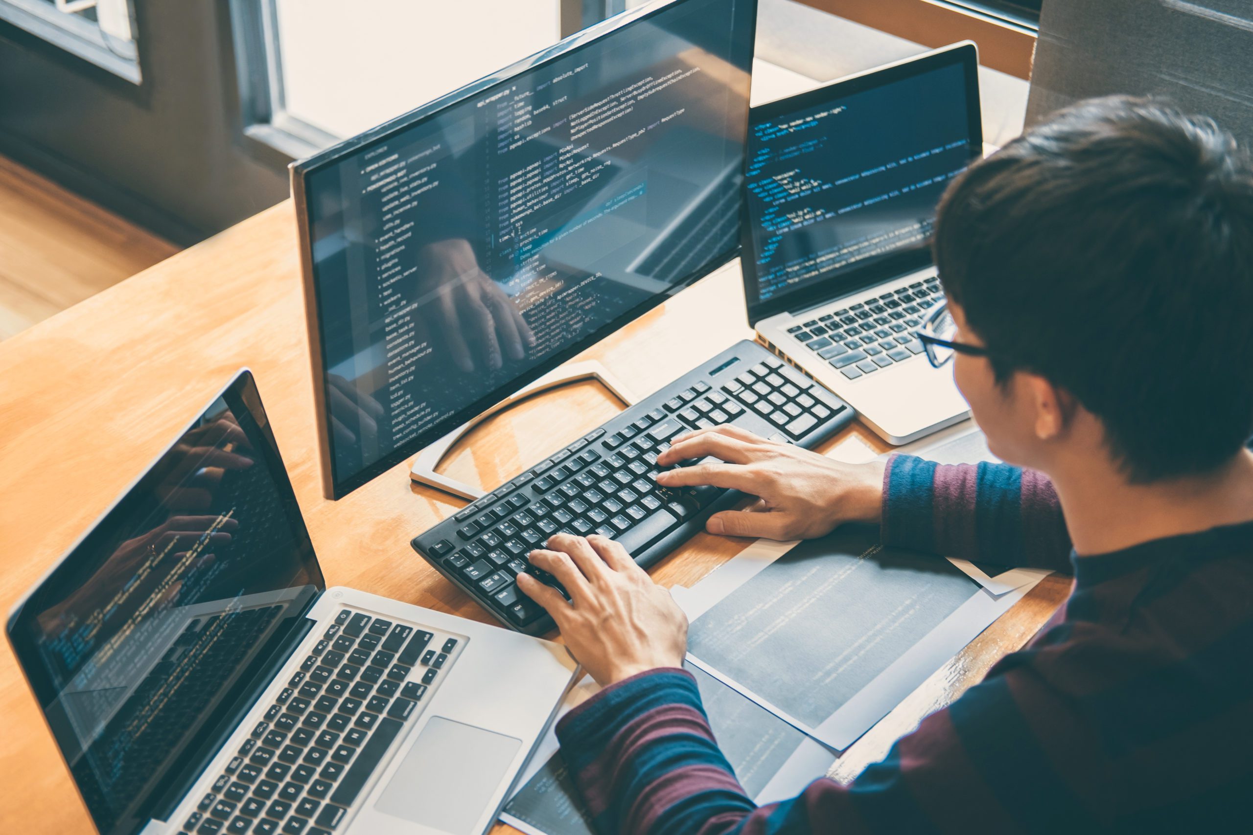 man with glasses working on two laptops and a monitor