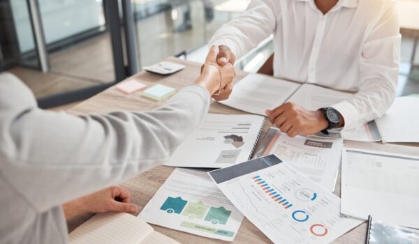 Two people shaking hands over desk.